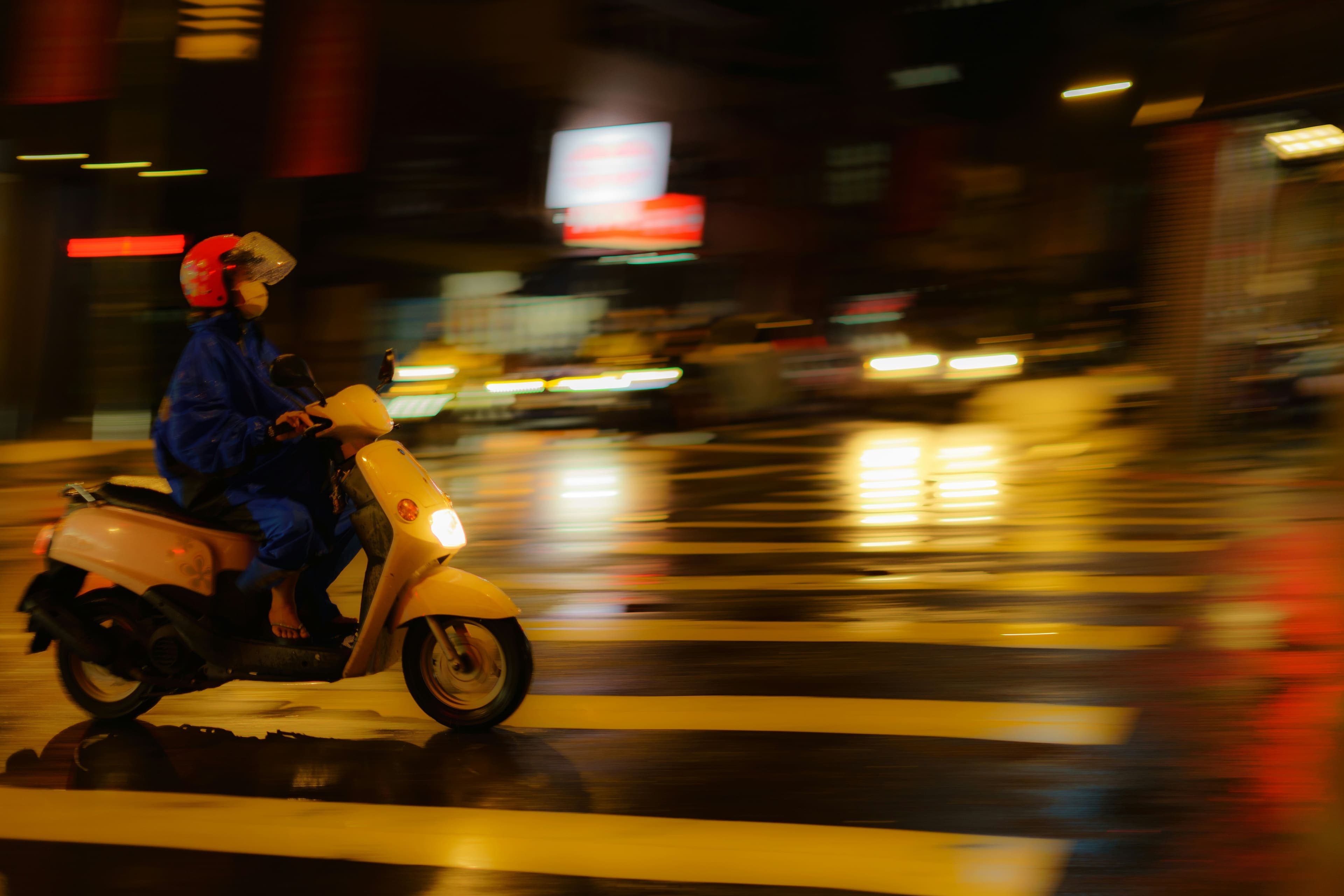 Gece yağmurlu caddede scooter süren biri
